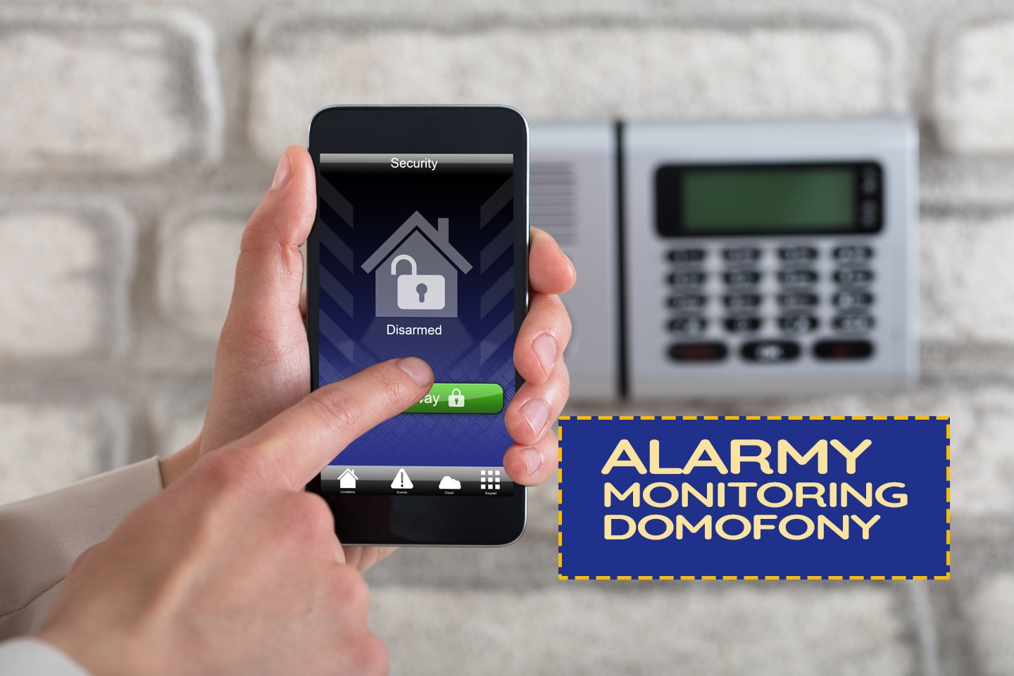 Osoba obsługuje aplikację do sterowania systemem alarmowym na smartfonie, w tle klawiatura alarmowa na ścianie z cegły.
