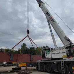 Żuraw samojezdny marki Demag Foselev podnosi element konstrukcji stalowej na placu budowy w pochmurny dzień.
