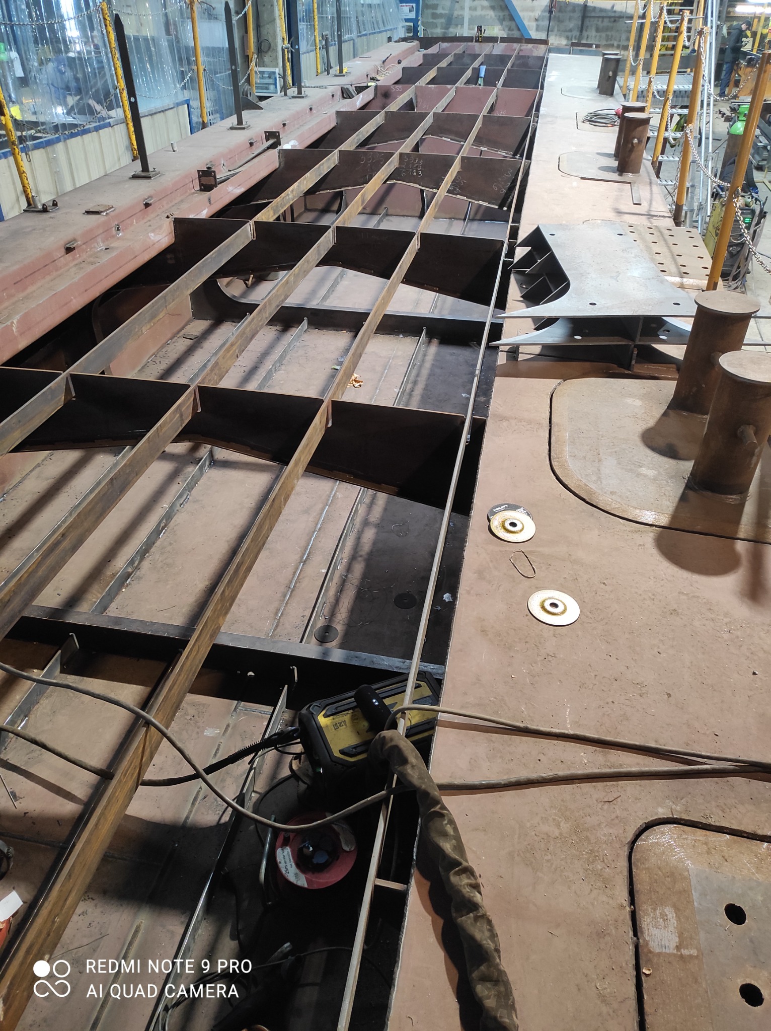 Konstrukcja stalowa w trakcie budowy, widoczne elementy spawane, narzędzia pracy i rękawica ochronna.