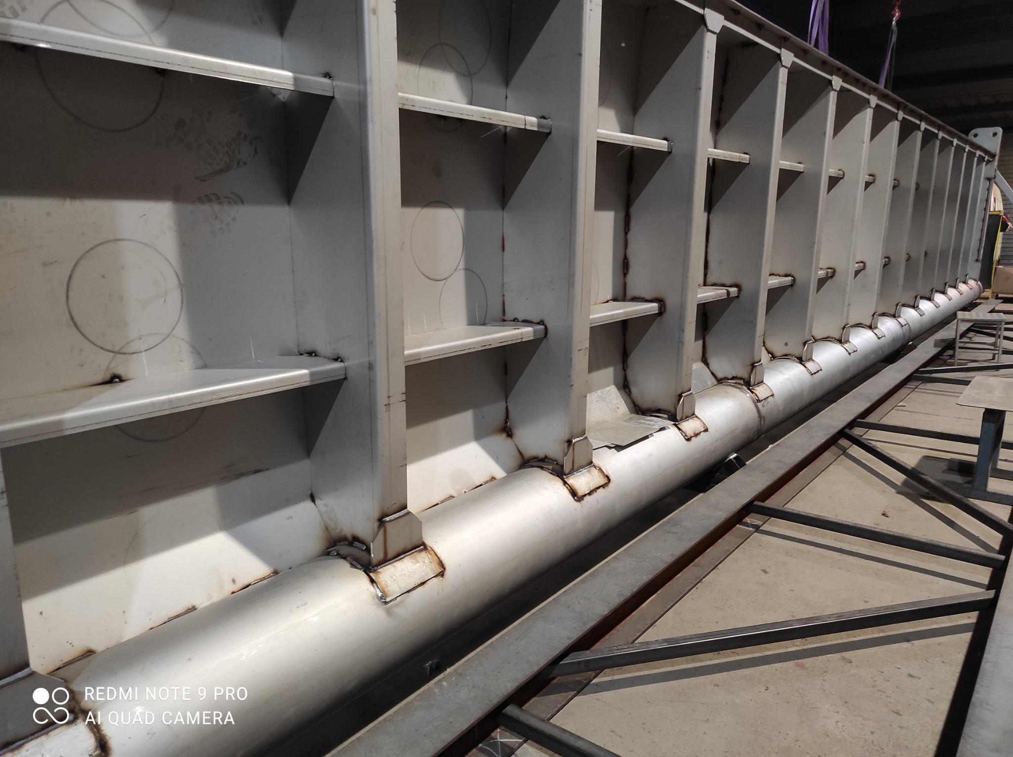 Wnętrze stalowej konstrukcji hali w trakcie budowy, widoczne spawy i elementy nośne, zarysowane okręgi na ścianach.