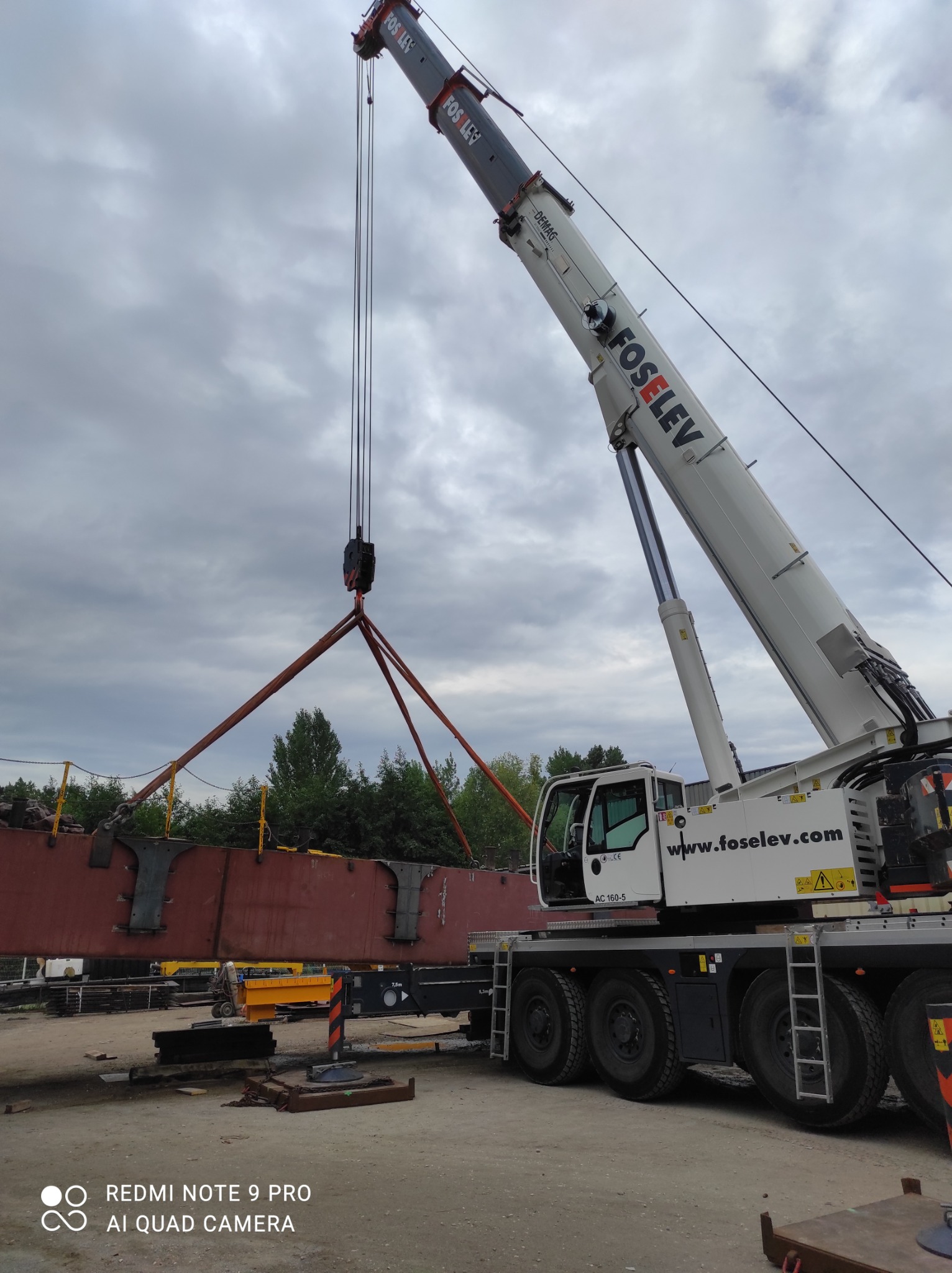 Żuraw samojezdny marki Demag Foselev podnosi element konstrukcji stalowej na placu budowy w pochmurny dzień.
