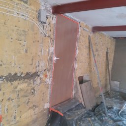 Firma Remontowo - Budowlana PLATRES Rafał Goc - Przygotowanie do tynkowania: surowa ściana z widocznymi instalacjami elektrycznymi, zabezpieczona folią podłoga i osłonięte drzwi. Widoczne poziomice i stalowa belka stropowa.