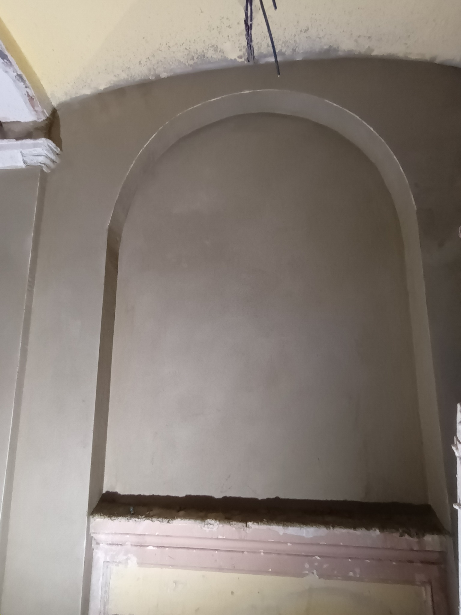 Wnęka z łukiem po nałożeniu gładzi, widoczne detale sztukaterii i fragment sufitu. Świeżo położona warstwa tynku o jednolitej strukturze.