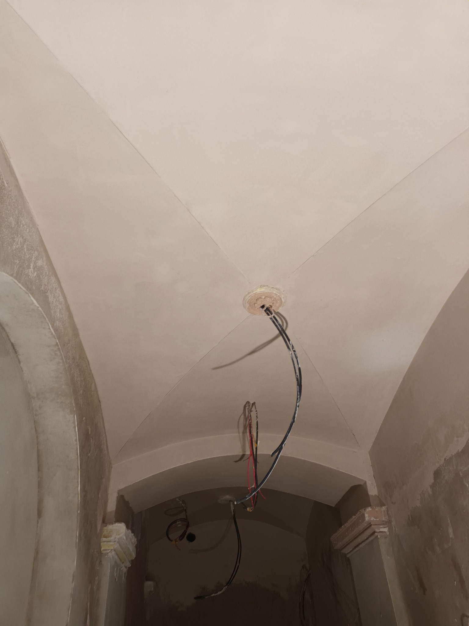 Wnętrze po tynkowaniu: łukowate przejście, gładki sufit z instalacją elektryczną. Widoczne ślady prac wykończeniowych przy łuku. Jasne, neutralne barwy.