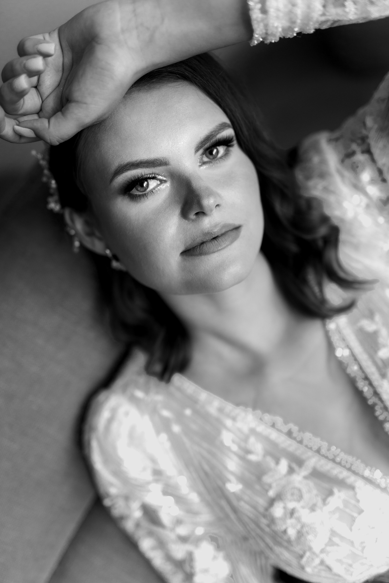 Portret kobiety w koronkowym stroju, leżącej z ręką na czole, w czerni i bieli. Ujęcie z góry podkreśla makijaż i wyrazistość spojrzenia.