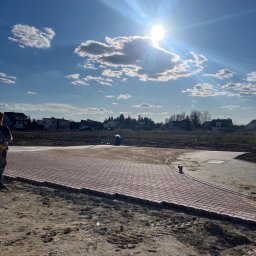 PoliTech - Częściowo ułożona, czerwona kostka brukowa na posesji z widocznym pracownikiem i błękitnym niebem z chmurami w słoneczny dzień.