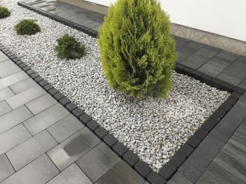 Szara kostka brukowa ułożona wokół rabaty z jasnymi kamieniami i ozdobnymi krzewami iglastymi, widok z góry.