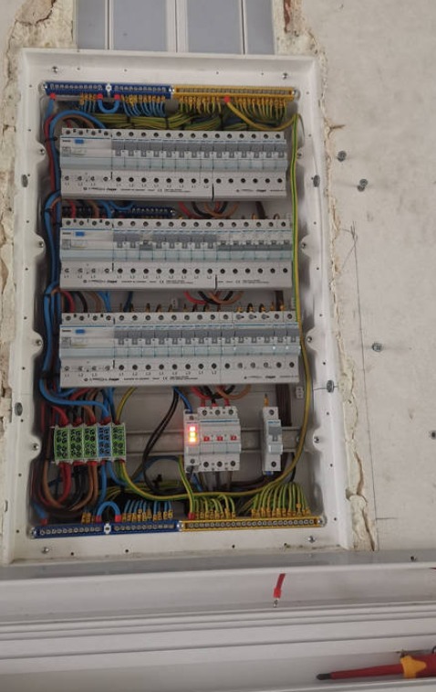 Rozdzielnia elektryczna wnękowa z zabezpieczeniami, okablowaniem i listwami, zamontowana w ścianie z widocznymi śladami prac wykończeniowych.