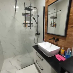 Nowoczesna łazienka z kabiną prysznicową typu walk-in, marmurowymi płytkami, czarną armaturą i szafką z umywalką nablatową, odbicie kabiny w lustrze.