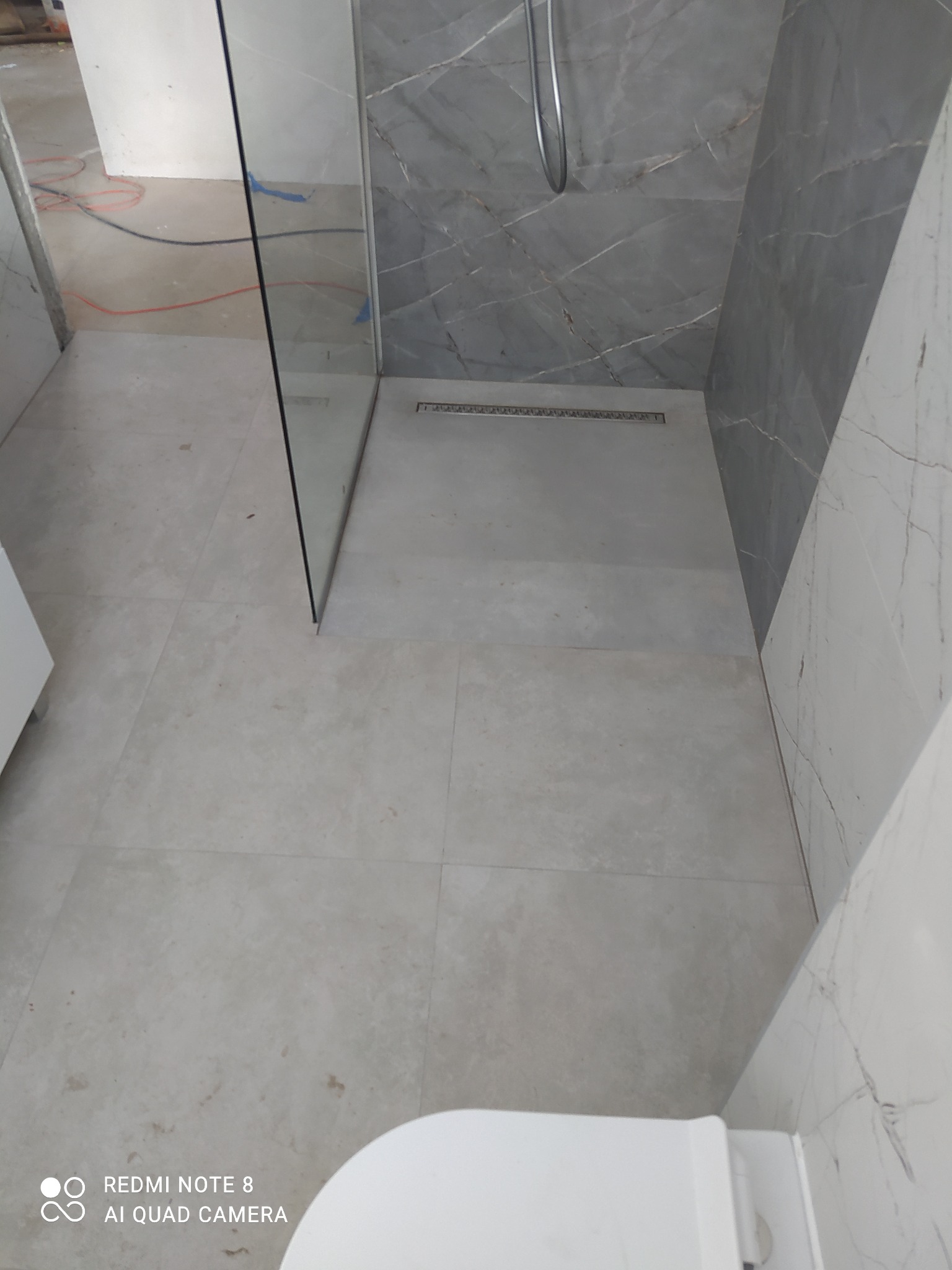 Wykończona łazienka z kabiną prysznicową typu walk-in, szare płytki imitujące marmur na ścianach i podłodze, odpływ liniowy w posadzce.