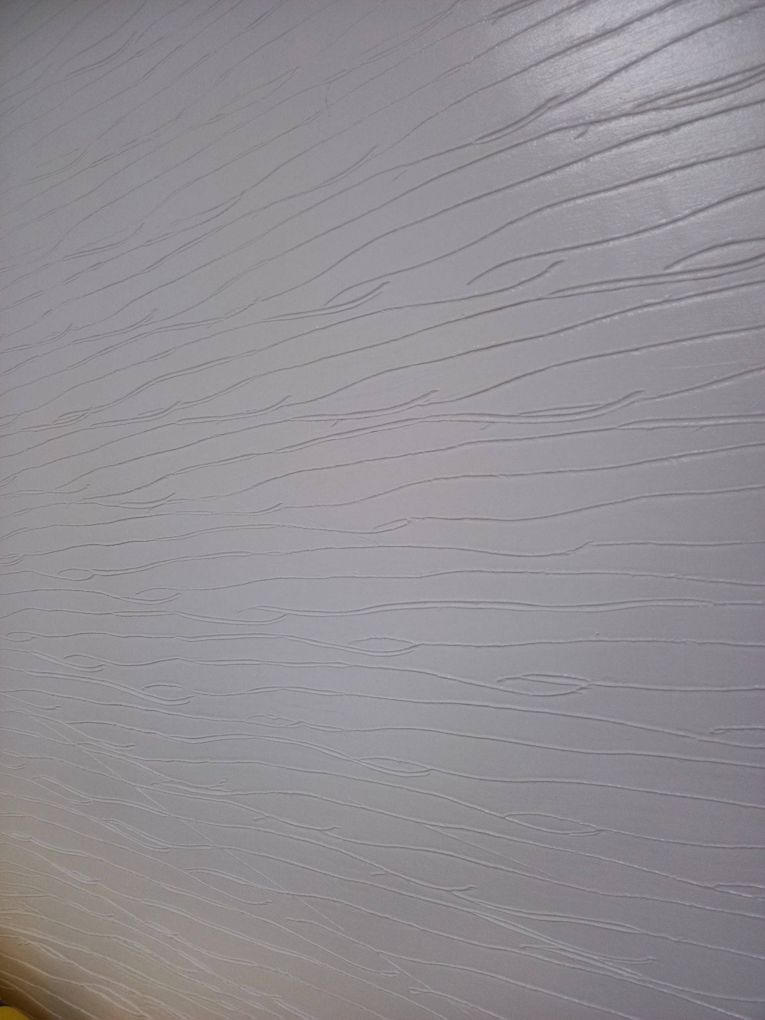 Jasnoszara ściana z dekoracyjną, poziomą fakturą przypominającą rysunek słojów drewna, delikatnie oświetlona z boku.