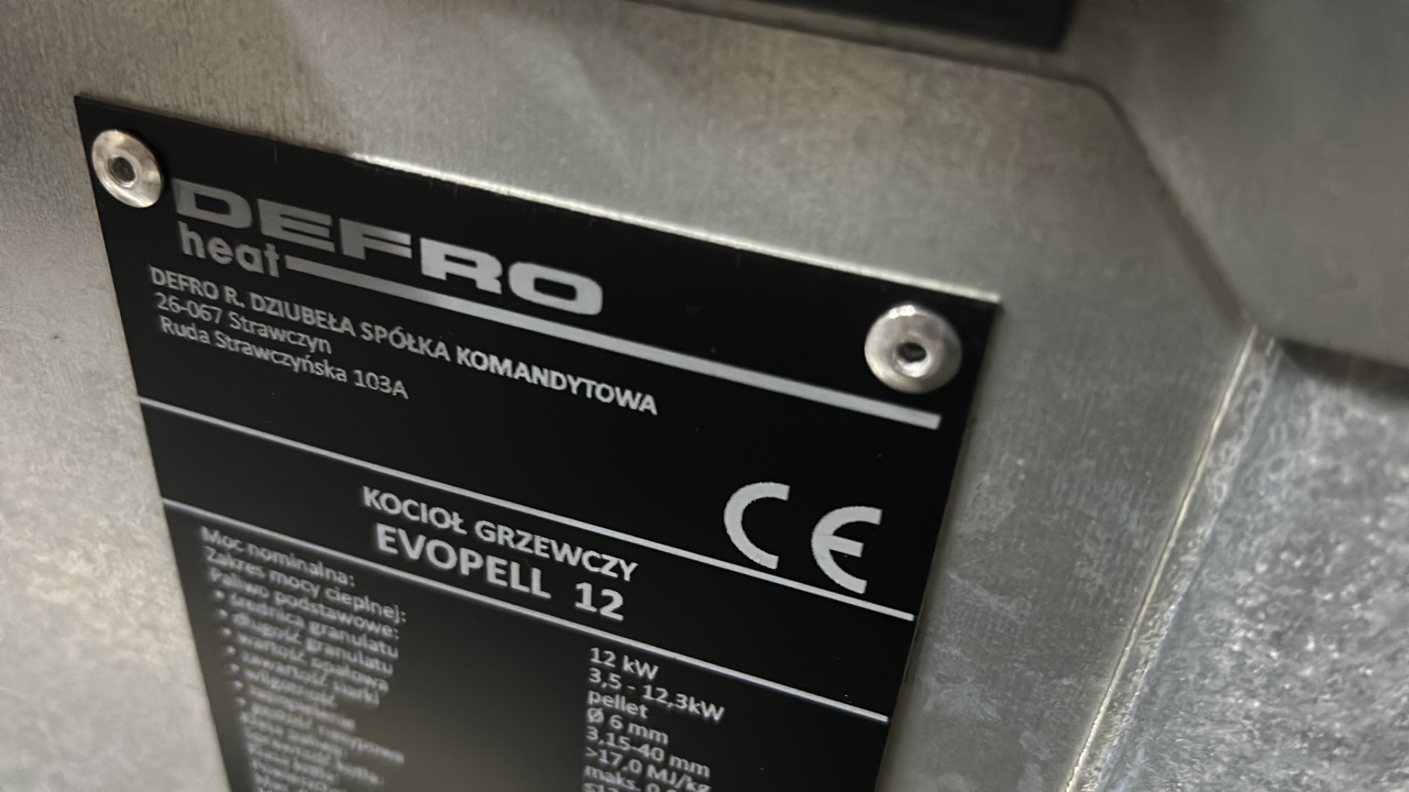 Tabliczka znamionowa kotła grzewczego Defro Evopell 12, z danymi technicznymi i adresem producenta, sfotografowana w Grudziądzu.