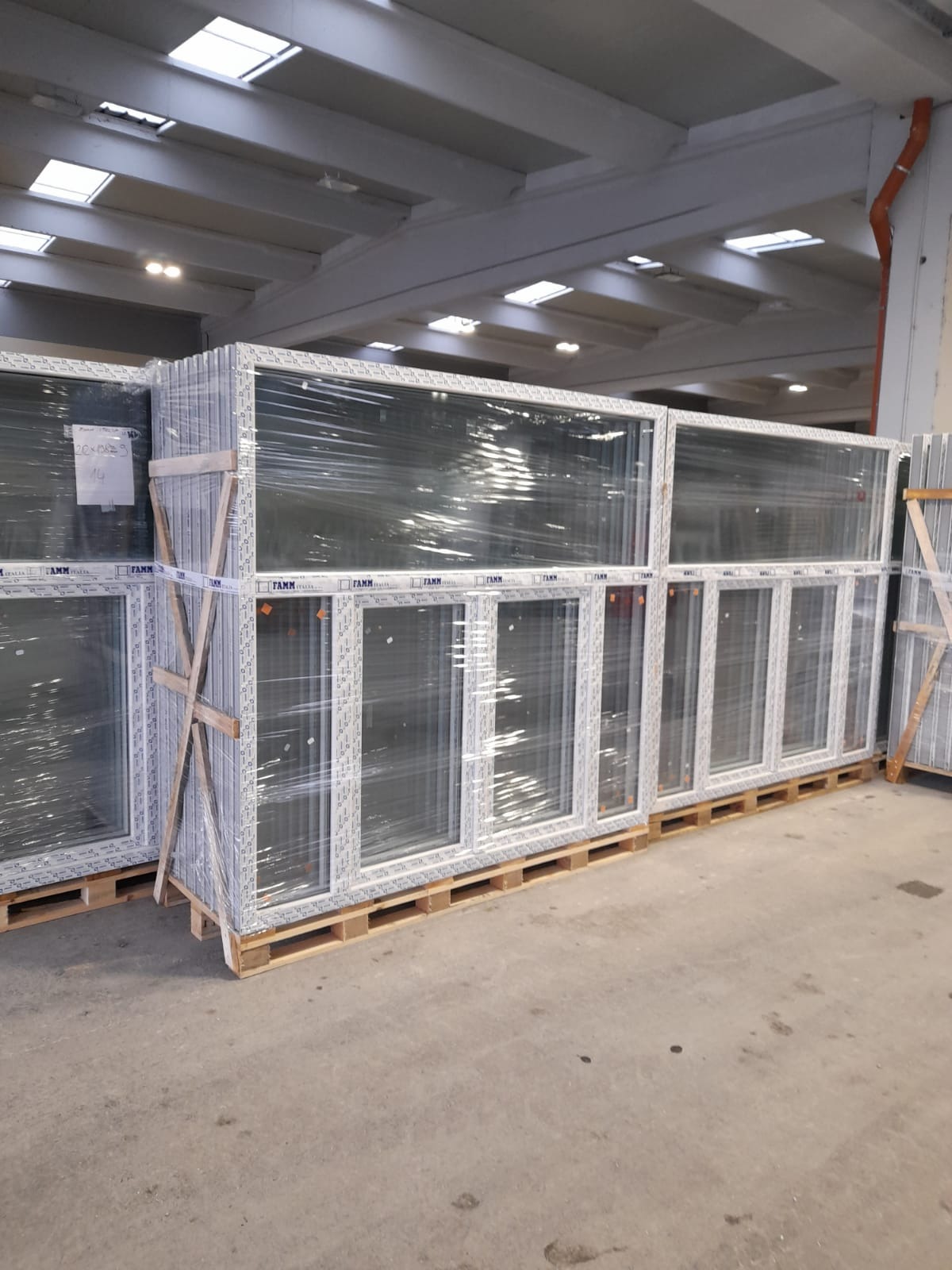 Magazynowane okna PCV, zabezpieczone folią i drewnianymi wspornikami, ułożone na paletach.