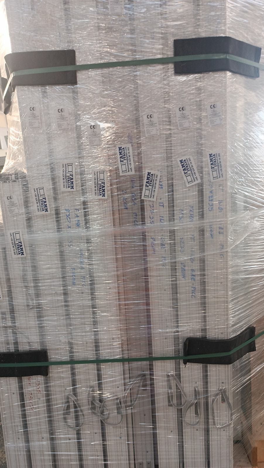 Paczka profili okiennych zabezpieczona folią stretch i taśmami, widoczne etykiety producenta FAMM ITALIA oraz odręczne notatki na profilach.