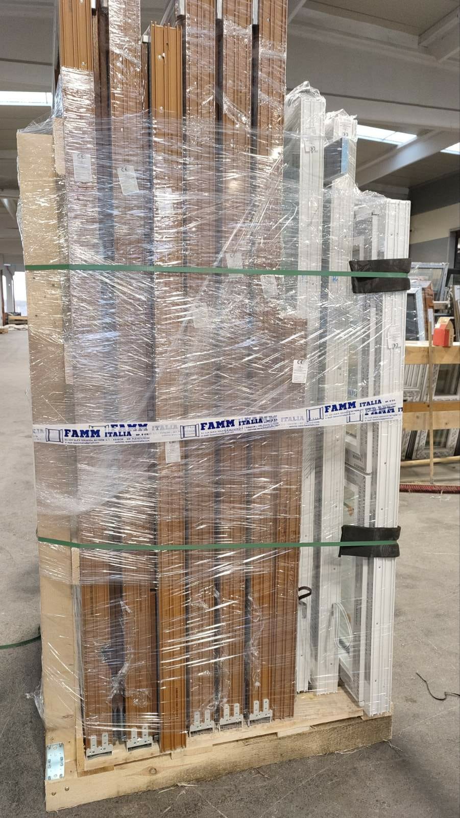 Paleta zafoliowanych okien w kolorze brązowym i białym, zabezpieczona pasami, widoczne logo producenta FAMM Italia.