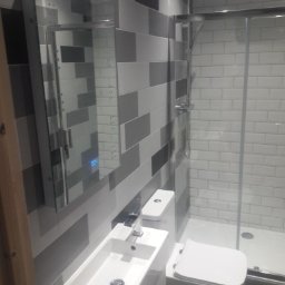 Krys-Mat - Nowoczesna łazienka z umywalką nablatową, toaletą i kabiną prysznicową, wykończona płytkami w odcieniach szarości i bieli, z lustrem z podświetleniem LED.