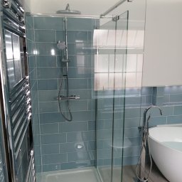 Krys-Mat - Nowoczesna łazienka z kabiną prysznicową typu walk-in, błękitnymi płytkami ułożonymi w cegiełkę, grzejnikiem drabinkowym i wolnostojącą wanną wypełnioną wodą.