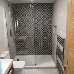 Krys-Mat - Nowoczesna łazienka po remoncie: kabina prysznicowa z wzorzystą ścianą, grzejnik drabinkowy, umywalka z szafką i toaleta.