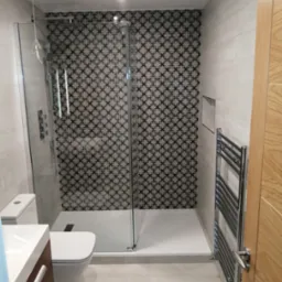 Nowoczesna łazienka po remoncie: kabina prysznicowa z wzorzystą ścianą, grzejnik drabinkowy, umywalka z szafką i toaleta.