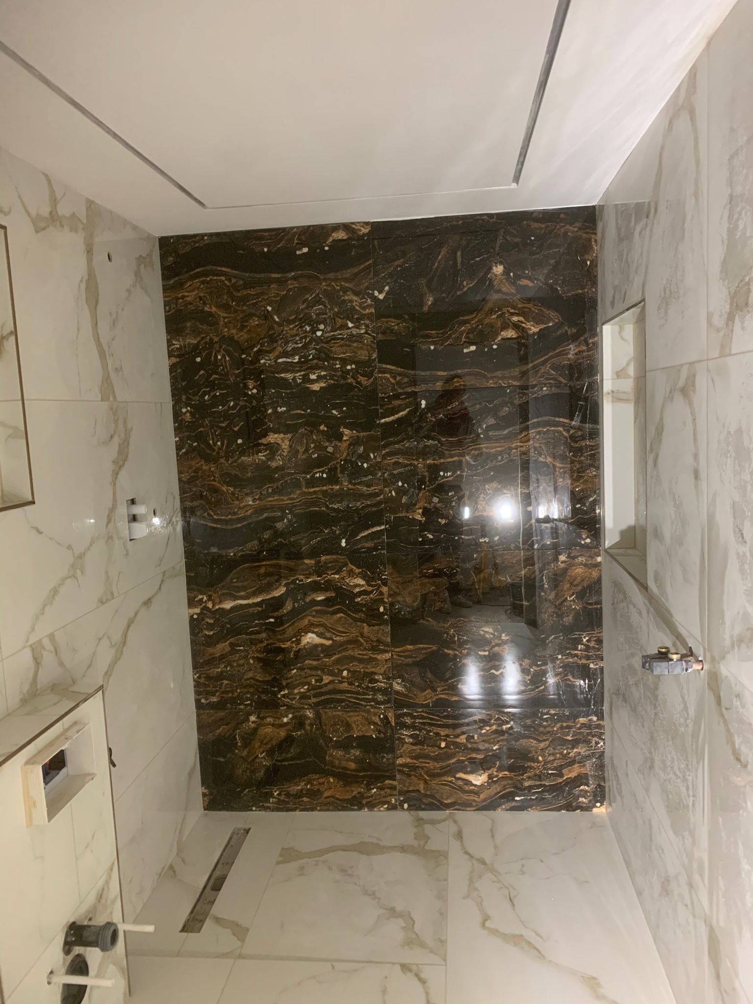 Nowoczesna łazienka z kontrastującymi płytkami: marmur carrara na ścianach i podłodze, oraz ciemnobrązowy marmur z wyraźnym użyleniem na jednej ze ścian.