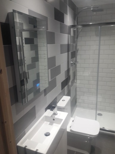 Nowoczesna łazienka z umywalką nablatową, toaletą i kabiną prysznicową, wykończona płytkami w odcieniach szarości i bieli, z lustrem z podświetleniem LED.