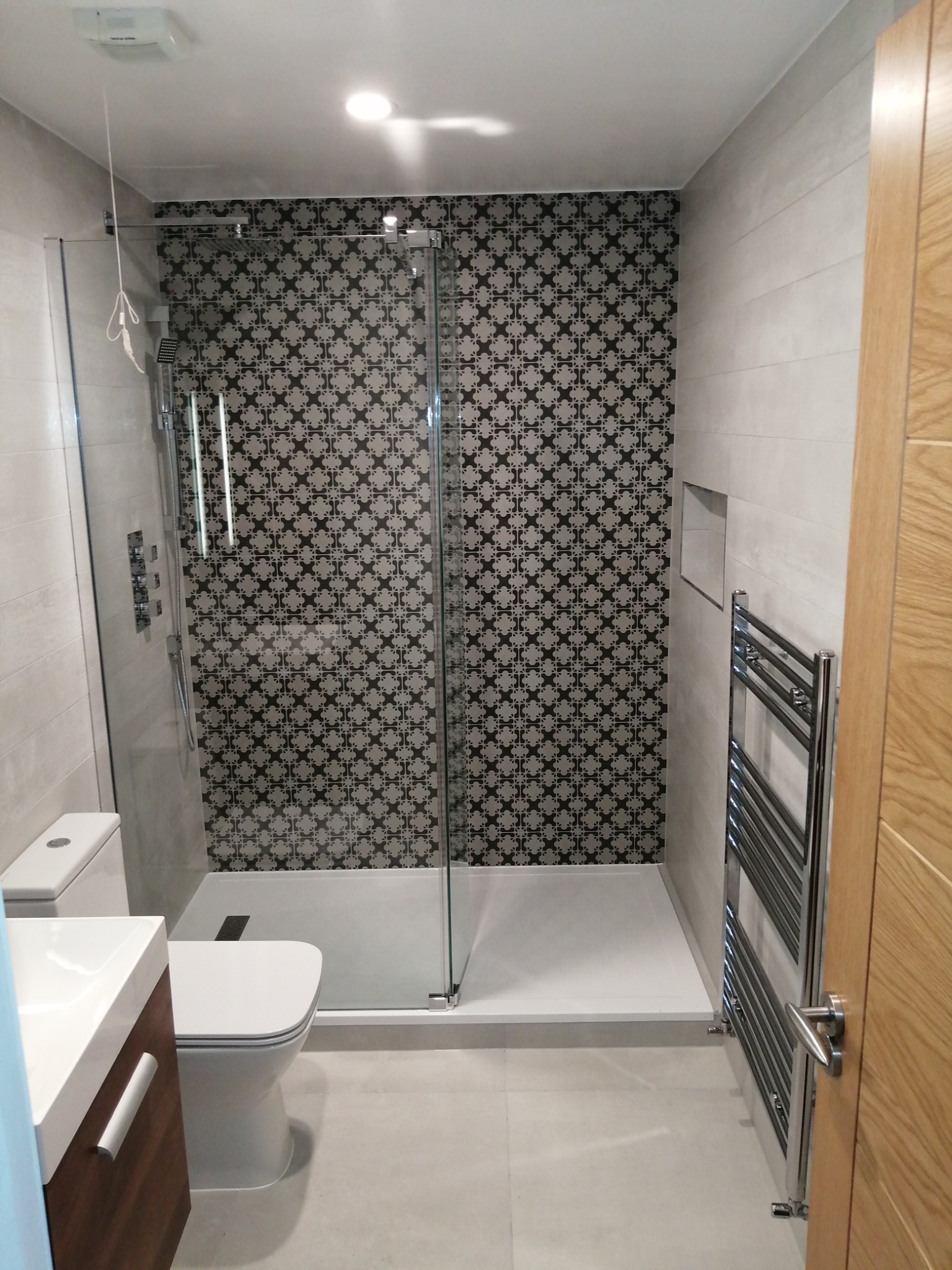 Nowoczesna łazienka po remoncie: kabina prysznicowa z wzorzystą ścianą, grzejnik drabinkowy, umywalka z szafką i toaleta.