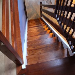 Usługi stolarskie Skupień - Nowoczesne schody drewniane z balustradą, widok z góry, naturalne oświetlenie podkreśla usłojenie drewna i geometryczny wzór balustrady.