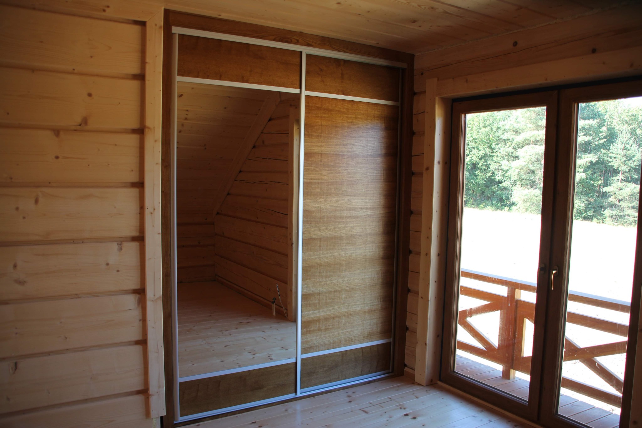 Drewniana szafa wnękowa z przesuwnymi drzwiami i lustrem w domu z bali.