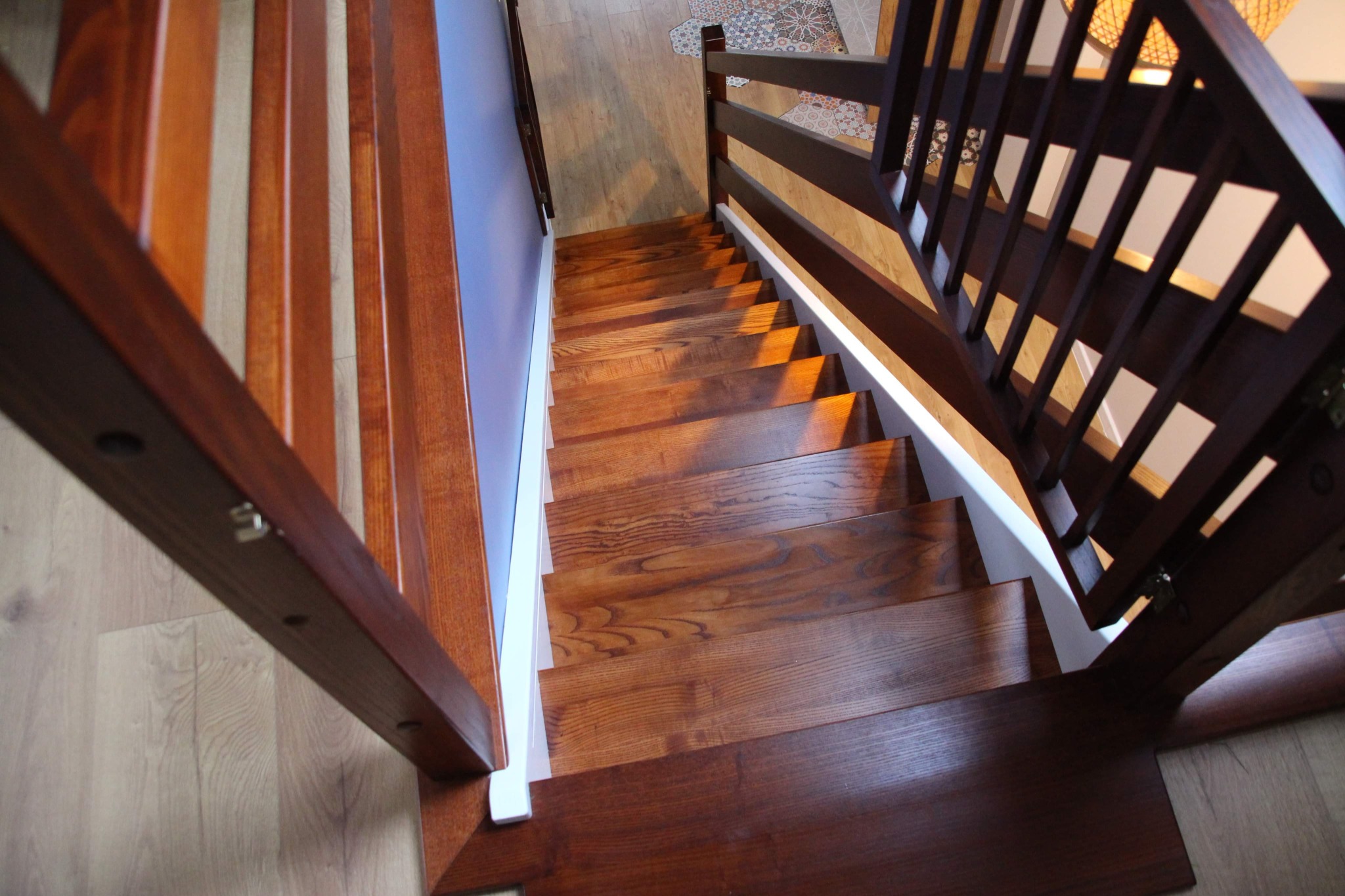 Nowoczesne schody drewniane z balustradą, widok z góry, naturalne oświetlenie podkreśla usłojenie drewna i geometryczny wzór balustrady.