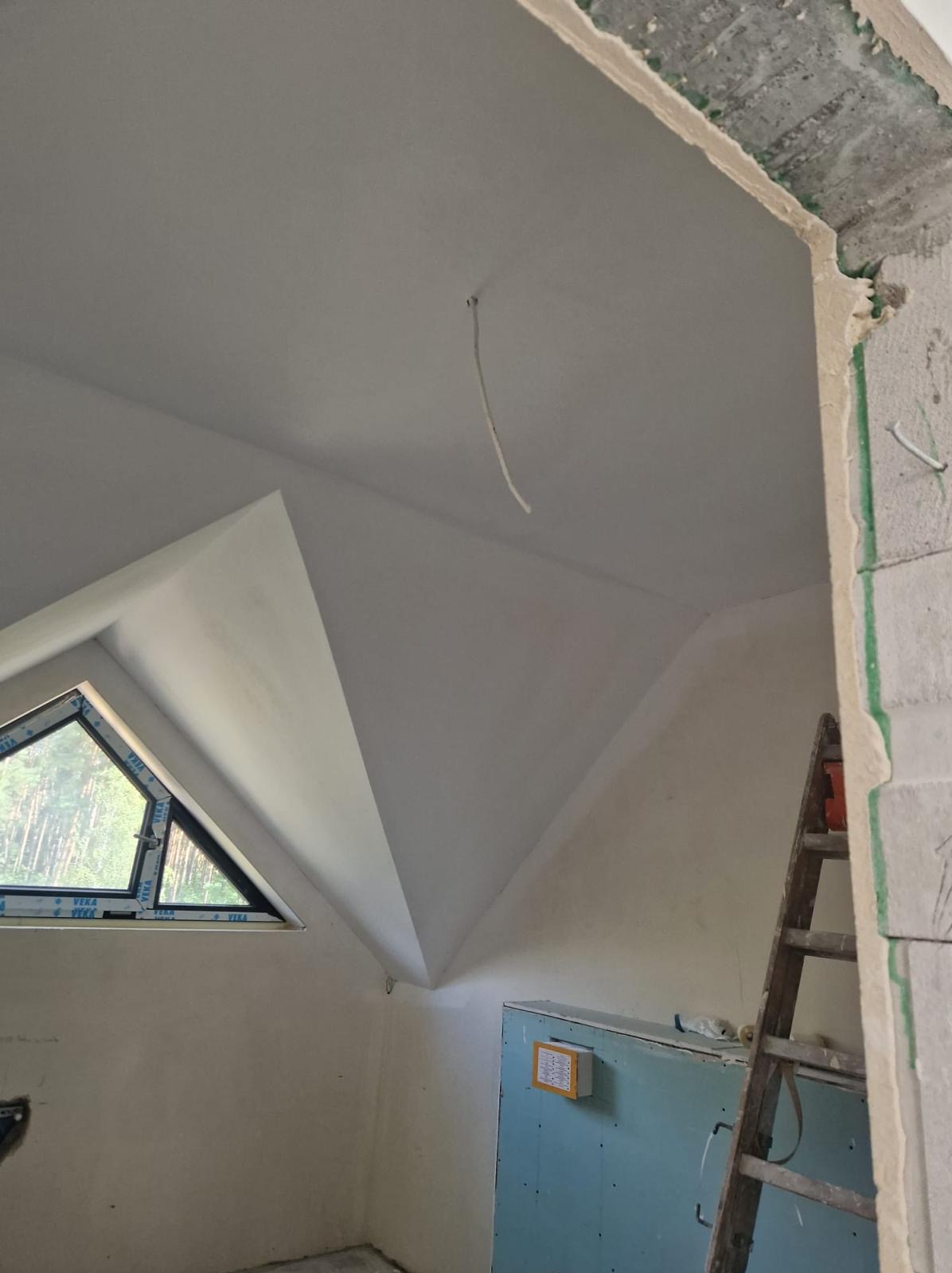 Poddasze po nałożeniu gładzi, widoczne okno trójkątne, wystający kabel ze ściany oraz drabina oparta o ścianę z bloczków.
