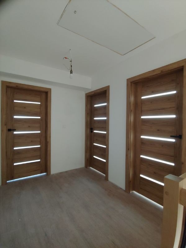 Trzy drewniane drzwi wewnętrzne z poziomymi przeszkleniami, zamontowane w nowym domu z jasnymi ścianami i drewnianą podłogą, widoczne niedokończone oświetlenie sufitowe.