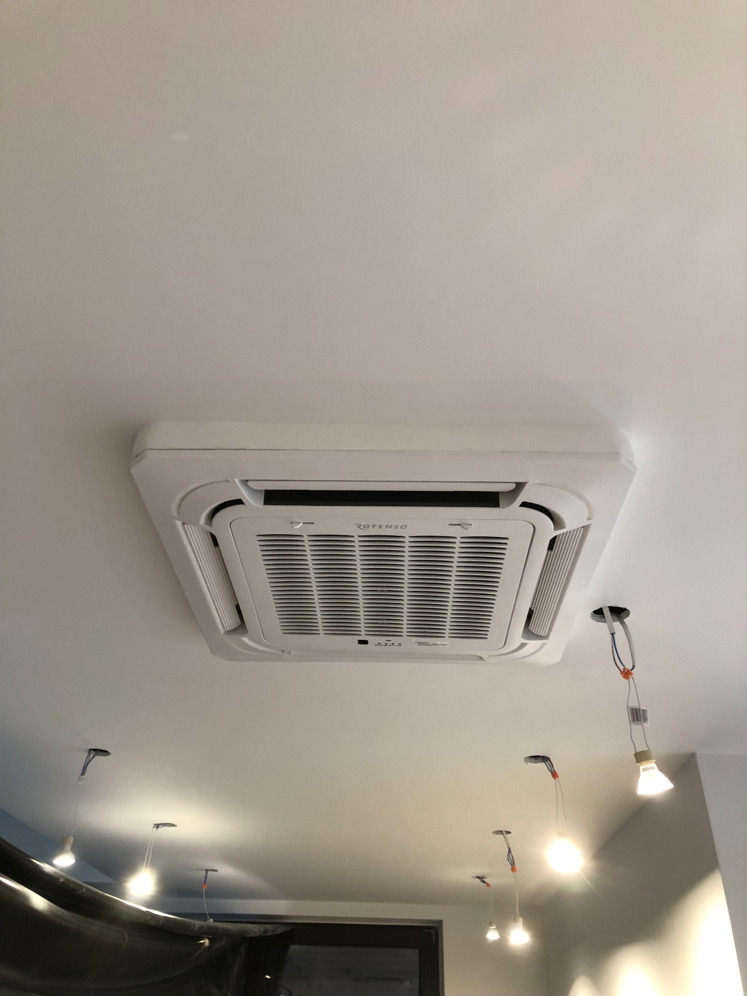 Kasetonowa jednostka wewnętrzna klimatyzacji ROTENSO zamontowana na suficie w Pisarzowicach, widoczne niedokończone instalacje elektryczne oświetlenia.