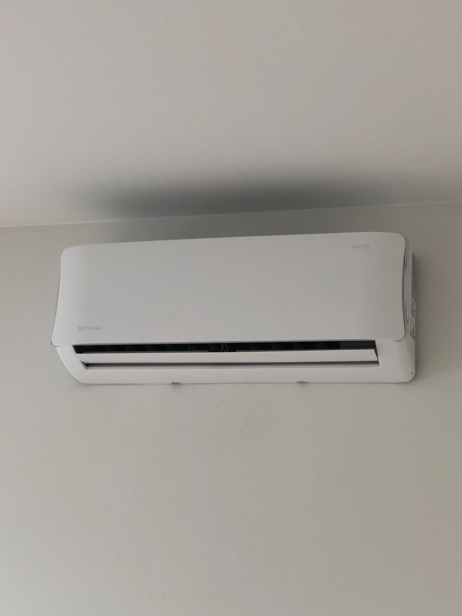 Biała jednostka klimatyzacyjna marki Rotenso zamontowana na jasnej ścianie, widoczna z lekkiego dołu.