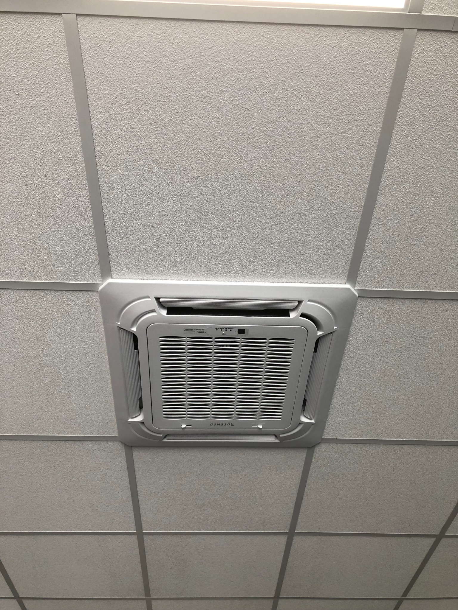 Sufitowy panel klimatyzacyjny Denso zamontowany w kasetonowym suficie biurowym, widok z dołu.