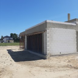 Oleksandr Ponchuk - Budowa domu z białych bloczków, widoczne podpory szalunkowe. W tle dom jednorodzinny i błękitne niebo. Stan surowy otwarty.