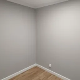Wnętrze pokoju po remoncie: szare ściany z białymi listwami przypodłogowymi i sufitowymi, panele podłogowe imitujące drewno, widoczne gniazdko elektryczne.