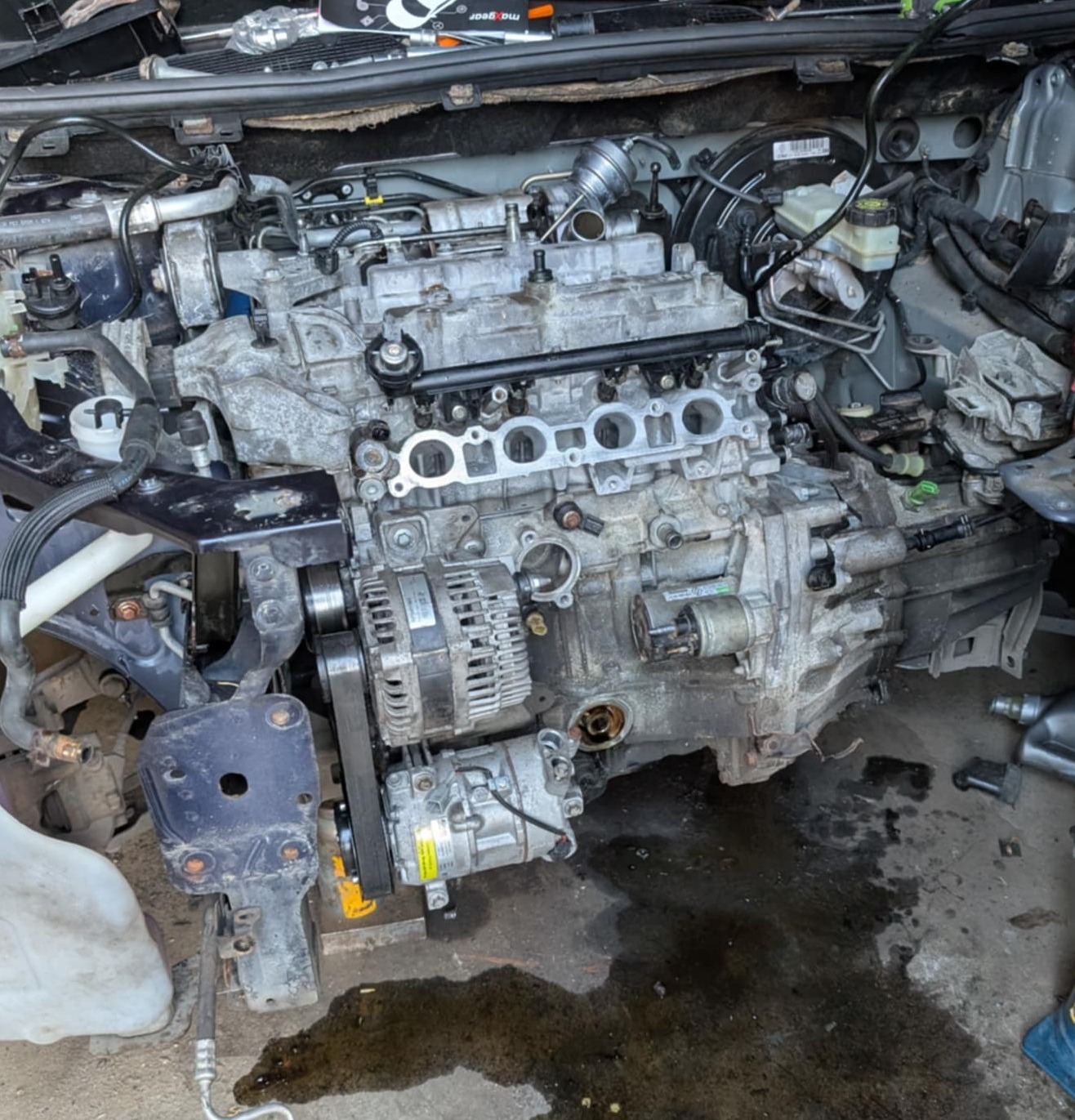 Wyjęty silnik samochodowy z widocznymi elementami osprzętu, umieszczony na podłożu warsztatowym z widocznymi śladami eksploatacji i narzędziami.