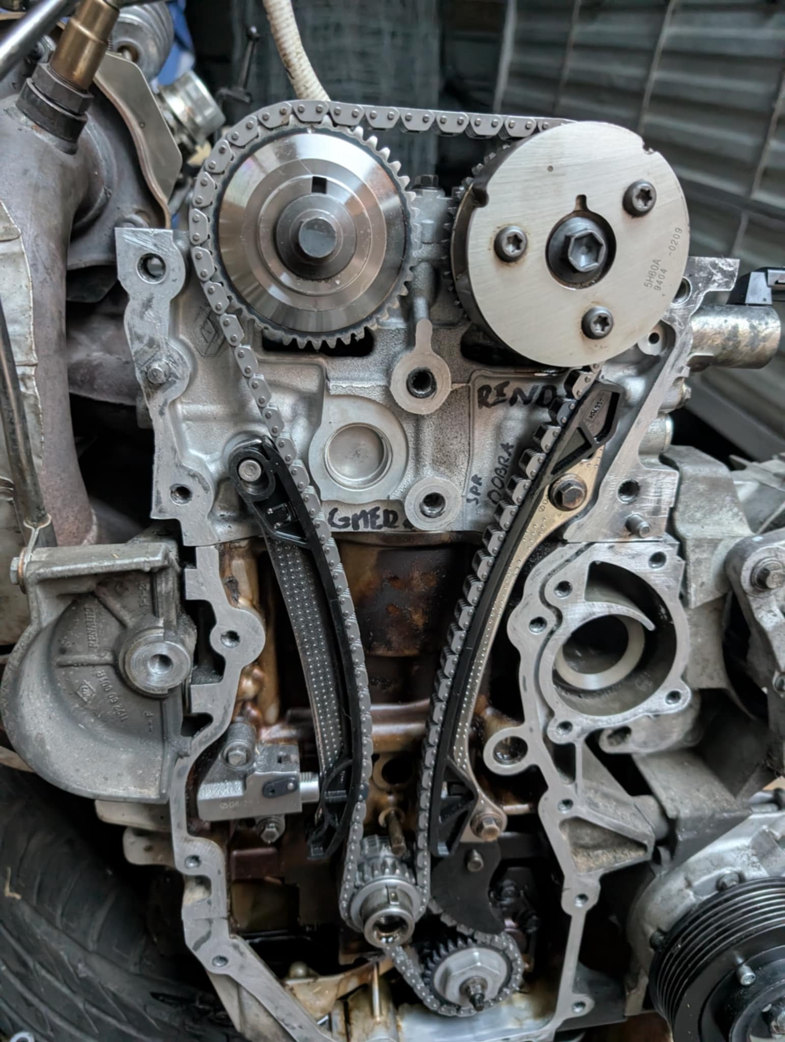 Odsłonięty silnik samochodowy z łańcuchem rozrządu, widoczne koła zębate i napisy 'RENO' oraz 'SPR DOBRA'. Detal mechaniki pojazdowej w warsztacie.
