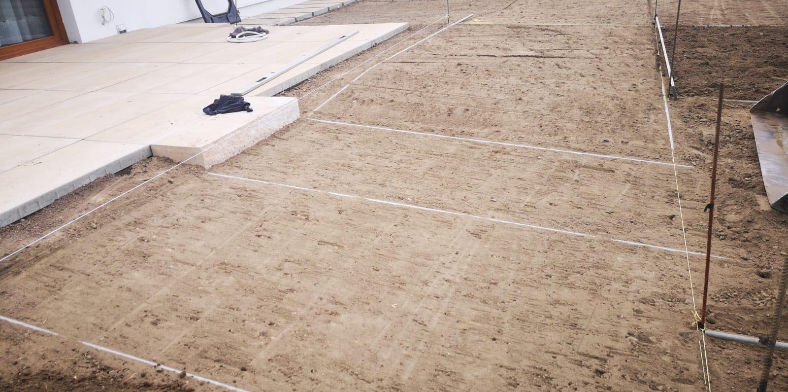 Przygotowany teren pod ogród z wytyczonymi liniami, widoczny fragment tarasu i narzędzia.