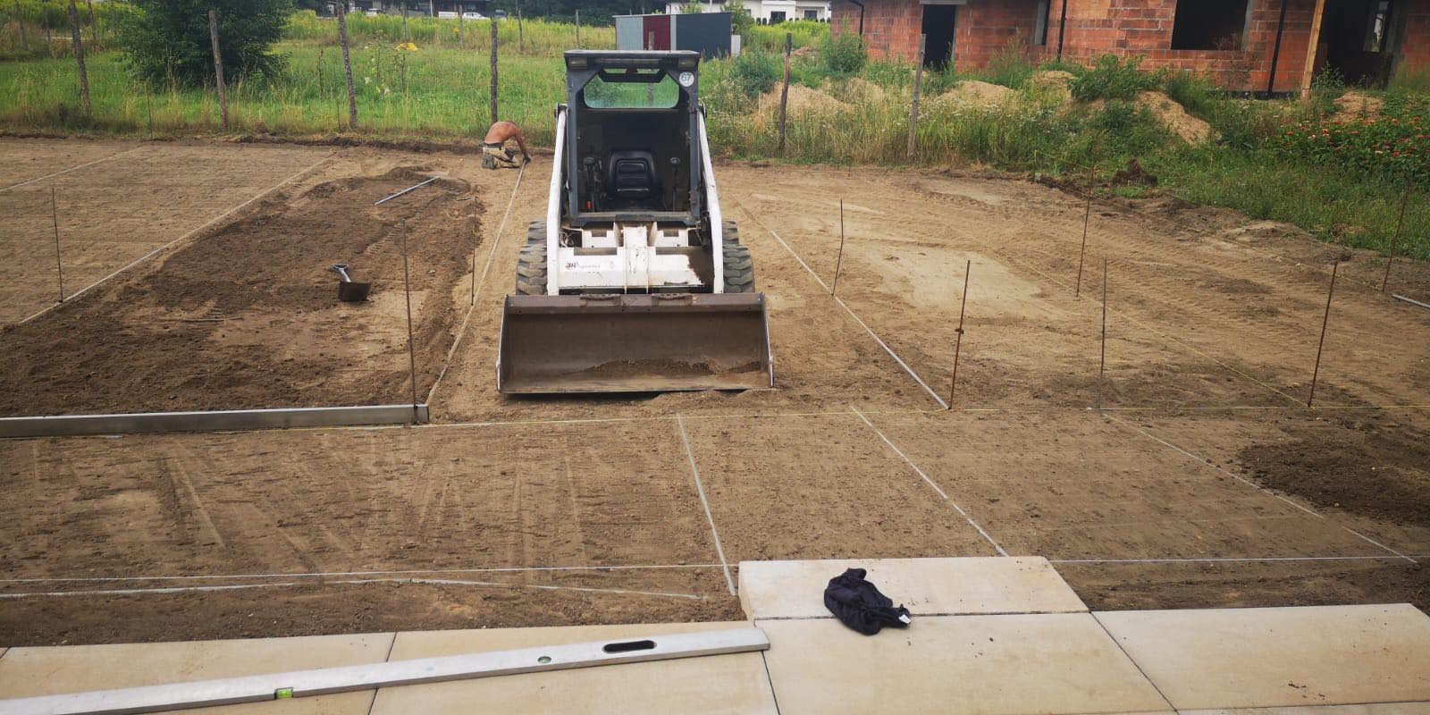 Przygotowanie terenu pod ogród z użyciem miniładowarki, widoczne wytyczone kwadraty, poziomica i pracownik w tle.