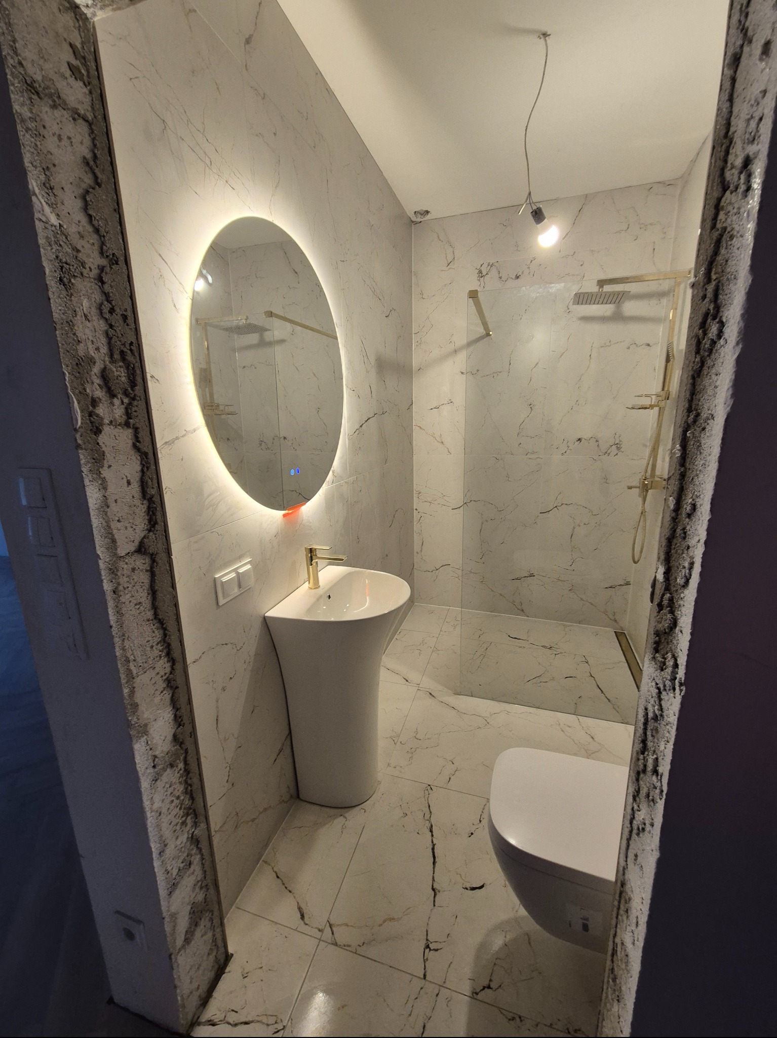 Nowoczesna łazienka w Lęborku z marmurowymi płytkami, podświetlanym lustrem i złotą armaturą. Kabina prysznicowa typu walk-in.