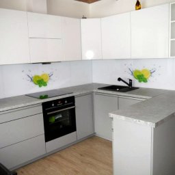 Michał Kopecki - Nowoczesna kuchnia z szarymi szafkami i białymi górnymi szafkami, blatem w kolorze betonu, czarnym zlewem i panelem szklanym z motywem cytryny i mięty.