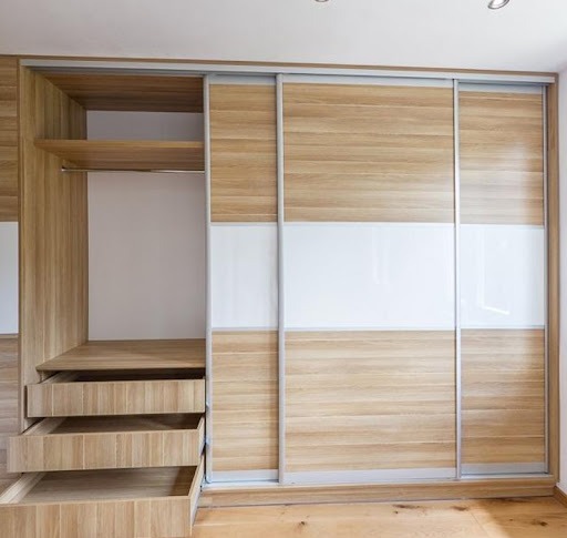 Jasna szafa przesuwna z drewnianymi frontami i białymi panelami, trzy szuflady wysunięte, widoczna półka i drążek na ubrania.