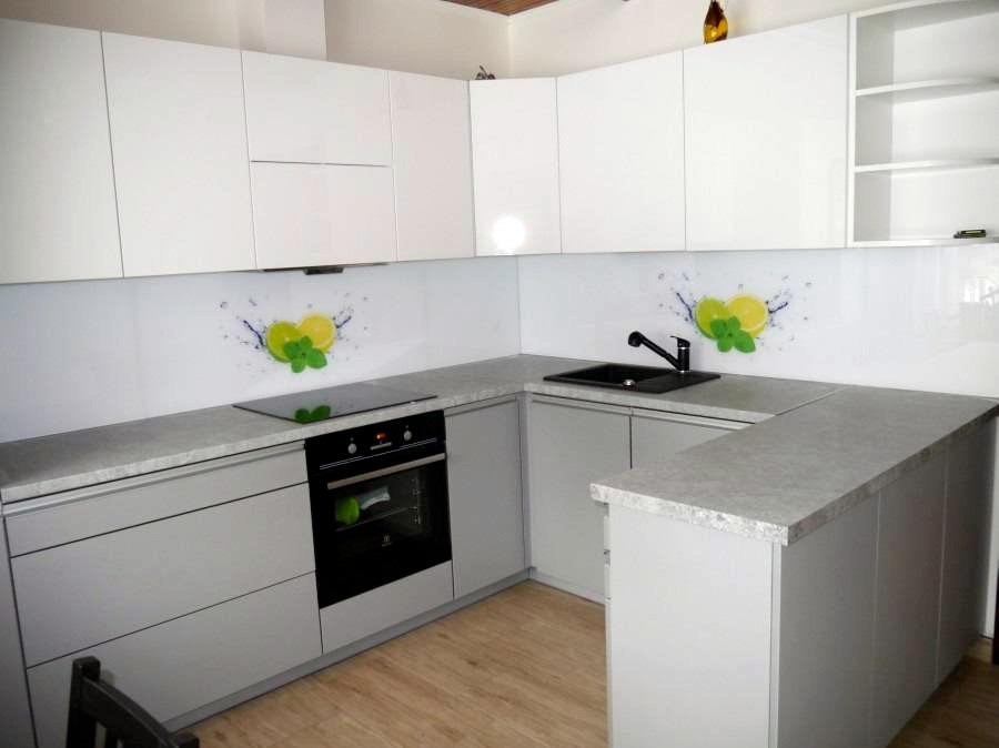 Nowoczesna kuchnia z szarymi szafkami i białymi górnymi szafkami, blatem w kolorze betonu, czarnym zlewem i panelem szklanym z motywem cytryny i mięty.