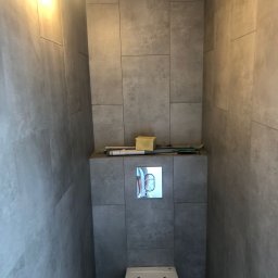 PO MAX - Nowoczesna toaleta w szarej łazience z dużymi płytkami, widoczny przycisk spłuczki i narzędzia na obudowie stelaża podtynkowego.