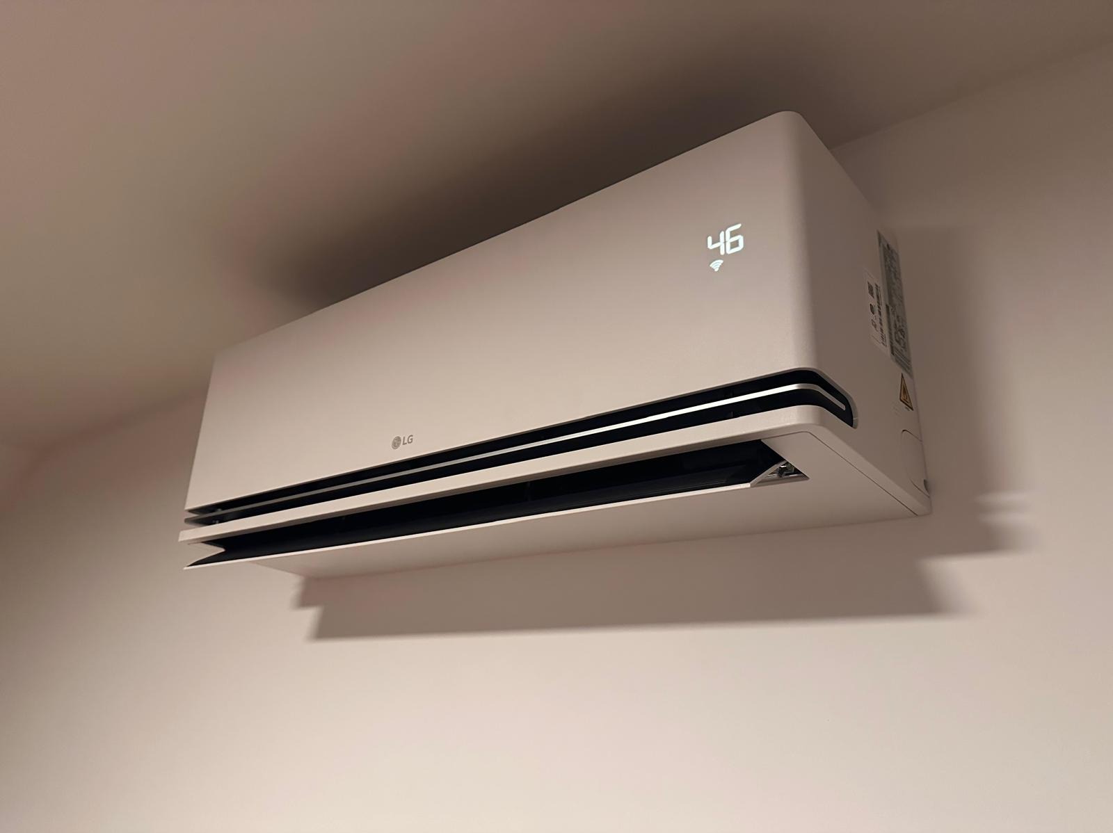 Nowoczesny, biały klimatyzator LG z wyświetlaczem temperatury 46 stopni Celsjusza, zamontowany na jasnej ścianie.