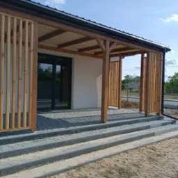 Nowoczesna pergola z drewnianymi lamelami, wsparta na kamiennych schodach, z widokiem na ogród w tle.