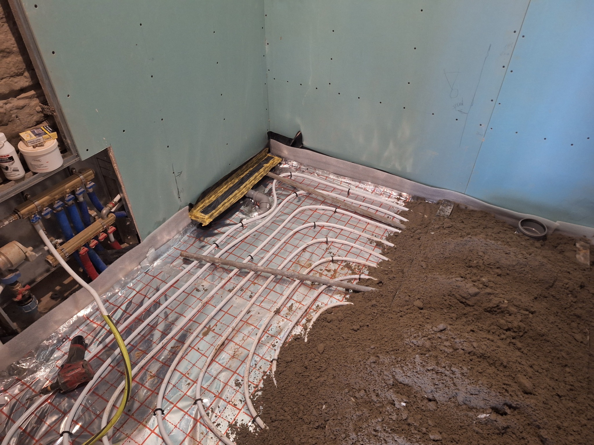 Montaż ogrzewania podłogowego w pomieszczeniu z płytami gipsowo-kartonowymi, widoczne rury i narzędzia, przygotowanie do wylewki.