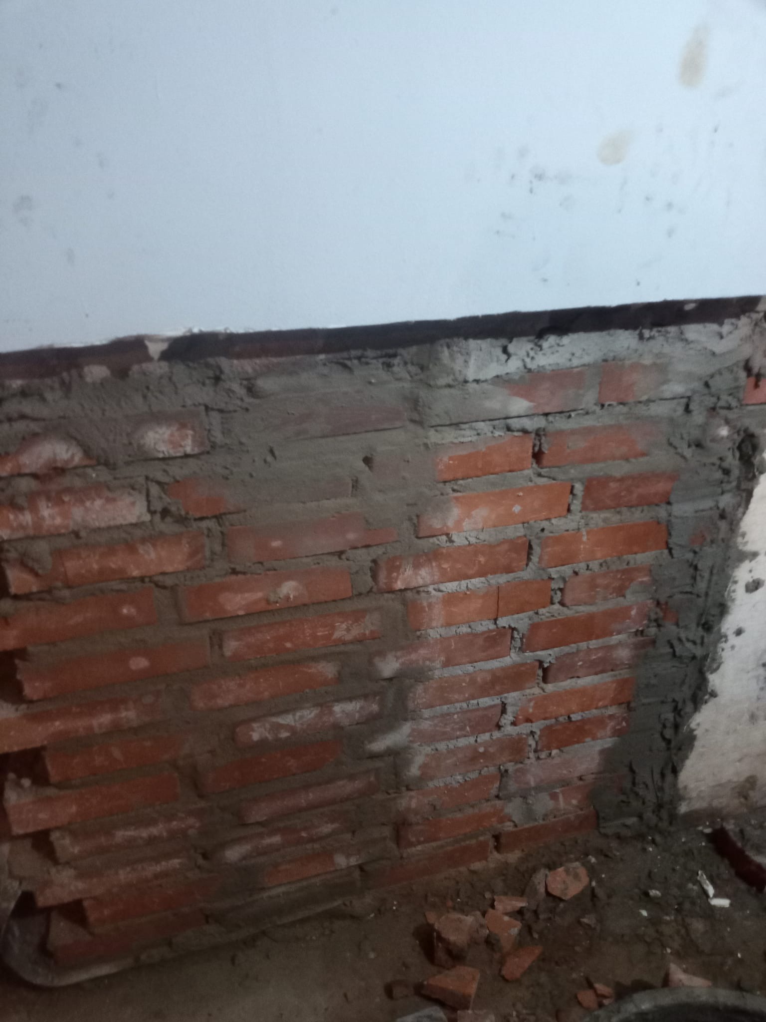 Murowana ściana z czerwonej cegły w trakcie prac w Nysie. Widoczne świeże spoiny i fragmenty gruzu. Dolna część ściany nieotynkowana.