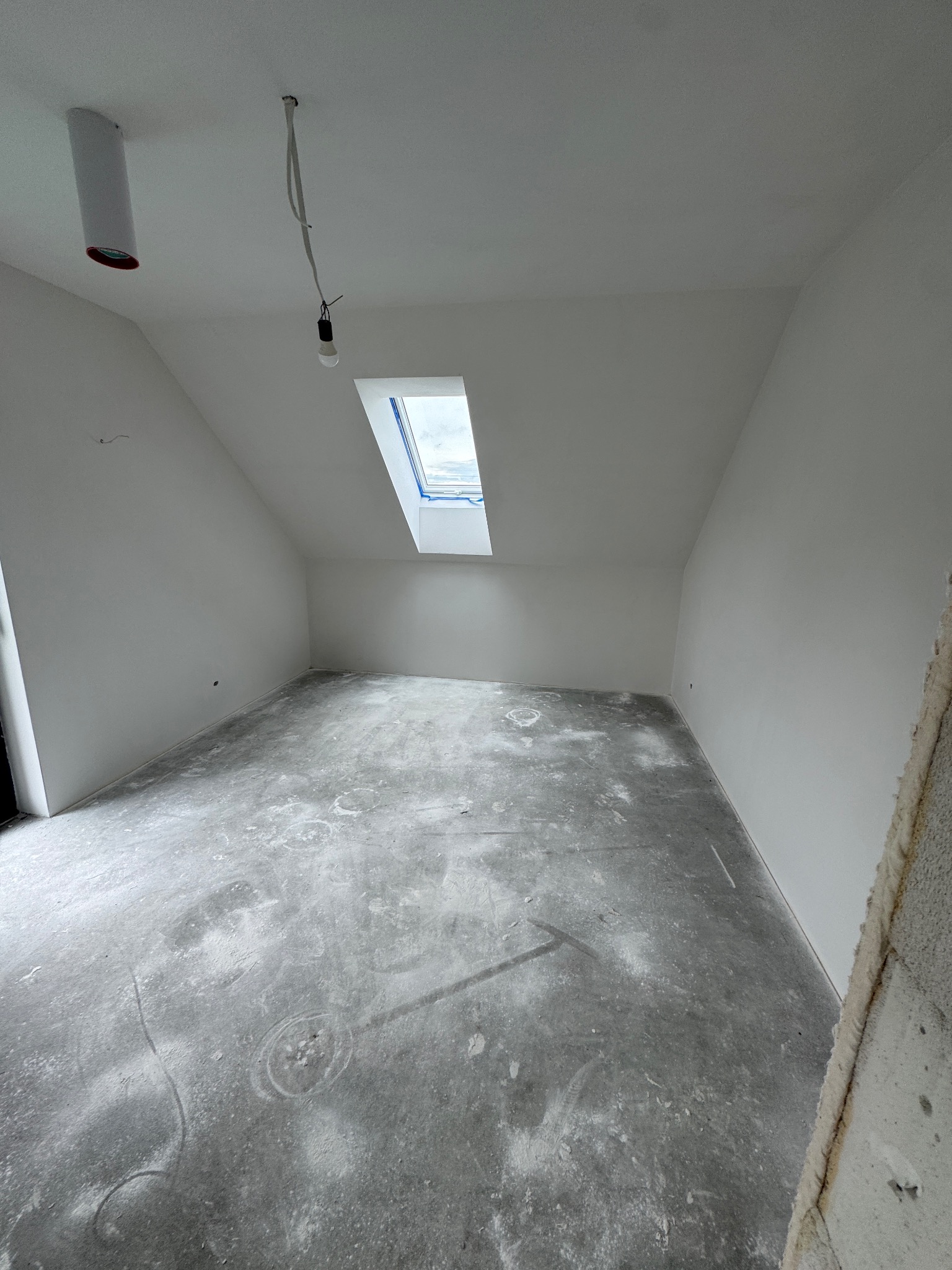 Poddasze w Radziechowach po gładziowaniu i malowaniu na biało. Widoczne okno dachowe, surowa podłoga i wystające przewody elektryczne.